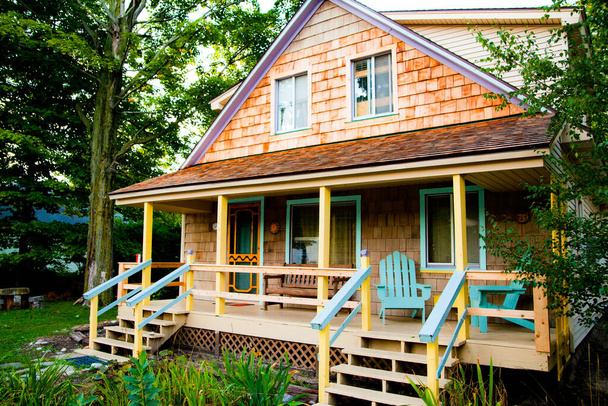 Encantadora casa de madera de dos pisos con cálidas tejas de cedro y un acogedor porche, rodeado de exuberante vegetación en Empire, Michigan. - Foto, imagen