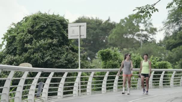 2人の若いアジアの女性の友人が公園で屋外で運動しながらリラックスして話す - 映像、動画