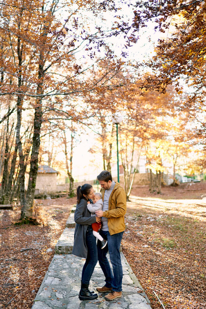 Papà sta accanto alla mamma a correggere una bambina tra le braccia su un sentiero nella foresta. Foto di alta qualità - Foto, immagini