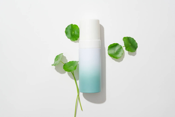 Centella asiatica leaves are decorated around an unbranded cosmetics bottle on a white background. Gotu kola has the ability to stimulate skin cell regeneration. - Photo, Image