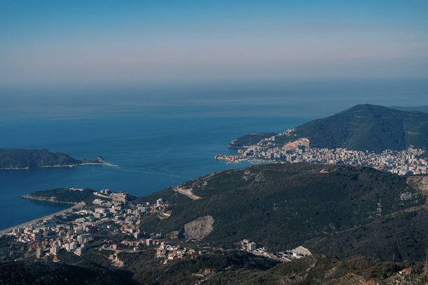 Dağın tepesinden, deniz kıyısındaki dağların eteklerindeki mavi gökyüzüne karşı yerleşim yerlerine bakın. Yüksek kalite fotoğraf - Fotoğraf, Görsel