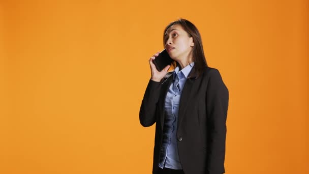 Businesswoman using smartphone to take remote call in studio, answering mobile phone and talking in front of camera. Female model with jacket having conversation with boss on device. - Footage, Video