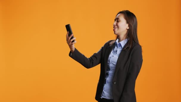 Filippiiniläinen työntekijä yhdistää verkossa video älypuhelimella, seisoo yli oranssi tausta. Nuori nainen itseluottamusta vastaamalla videoneuvotteluyhteys internetissä. - Materiaali, video