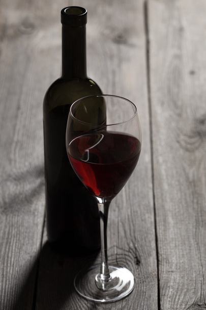 Red wine glass with bottle on wooden table - Valokuva, kuva