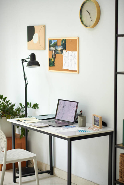 Рабочее место модного дизайнера с набросками ноутбуков и булавочной доской на стене - Фото, изображение