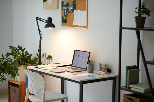 Bureau van fashion design student met laptop, lamp en moodboard aan de muur - Foto, afbeelding