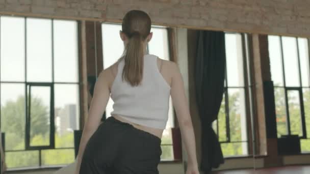 Visão traseira tiro de duas jovens dançarinas caucasianas vestindo roupas esportivas confortáveis realizando movimentos de dança contemporânea na frente de parede espelhada de comprimento total no estúdio de dança - Filmagem, Vídeo