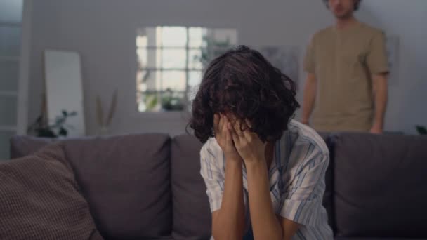 Enfoque selectivo de la mujer joven deprimida sentada en el sofá, mientras que la figura masculina estresantemente caminando de ida y vuelta en el fondo - Metraje, vídeo