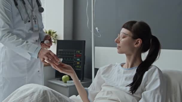 Střední záběr bělošky pacientky ležící v posteli a užívající předepsané pilulky od svého lékaře - Záběry, video
