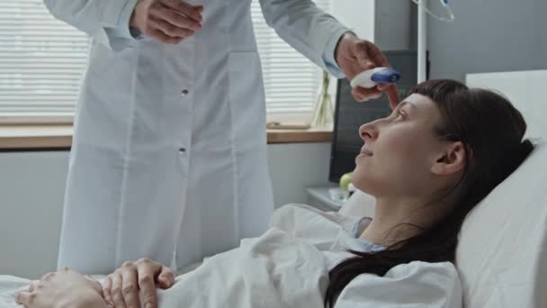 Střední detailní záběr ženského lékaře při měření teploty jejího bělošského pacienta s teploměrem - Záběry, video