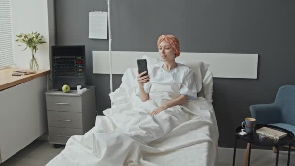 Zoom de paciente femenina con envoltura de cabeza acostada en cama de hospital que tiene video todo - Metraje, vídeo