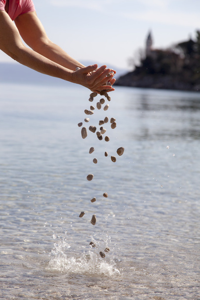 Hands dropping small stones in the sea - Photo, Image