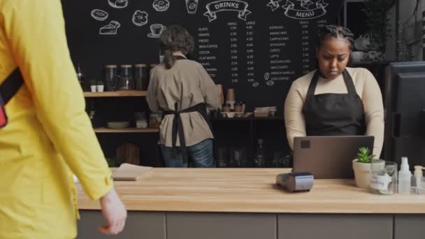 Delivery man coming in coffee shop while two female baristas preparing food order for him - Footage, Video