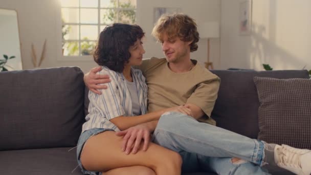 Tiro médio de jovem casal sentado no sofá abraçando uns aos outros, gentilmente falando uns com os outros - Filmagem, Vídeo