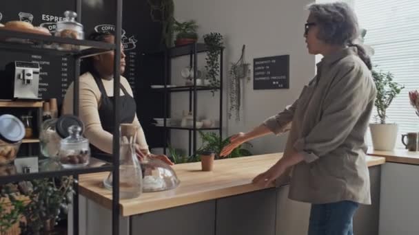 Klient z siwymi włosami narzekający na jej drinka do baristy za ladą w kawiarni - Materiał filmowy, wideo