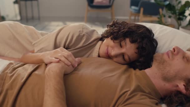 Μέτριο πλάνο του νεαρού παντρεμένου ζευγαριού ξαπλωμένο άνετα στο κρεβάτι, να κοιμάται κατά τη διάρκεια της ημέρας - Πλάνα, βίντεο