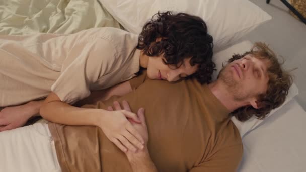 Nad głową ujęcie dwóch młodych ludzi leżących bardzo blisko siebie, śpiących razem w łóżku - Materiał filmowy, wideo