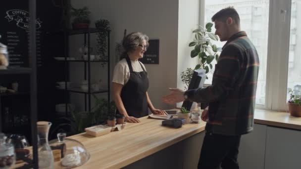 Muž zákazník platí za své jídlo pomocí digitálních hodinek na zápěstí, zatímco žena barista připravuje svou objednávku - Záběry, video