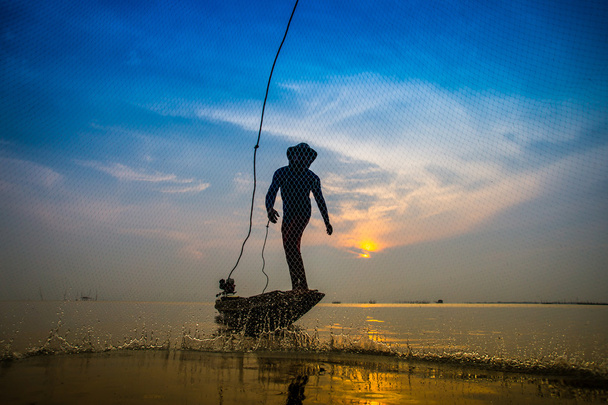 Silhouettes pêcheur jetant des filets de pêche au coucher du soleil
. - Photo, image