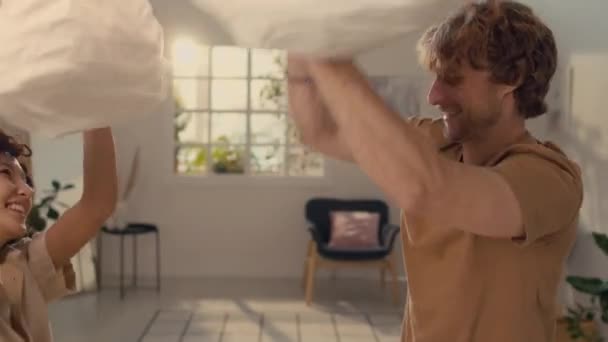 Zwei glückliche junge Verliebte in beigefarbenen Kleidungskissen kämpfen im Schlafzimmer - Filmmaterial, Video