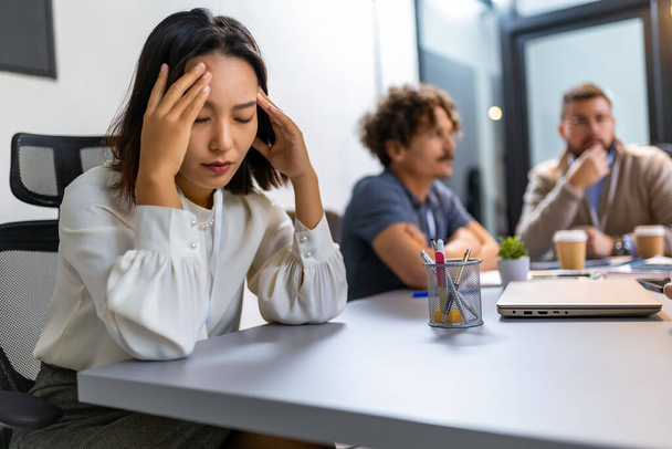 Giovane donna d'affari asiatica che ha mal di testa in ufficio mentre ha un incontro - Foto, immagini