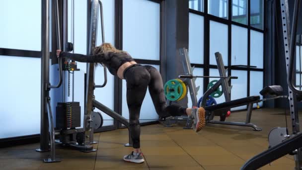 Atletik kız, kalça kaslarını ve kalça kaslarını kablolu kanalda çalıştırıyor. kablo kalçası uzantıları  - Video, Çekim