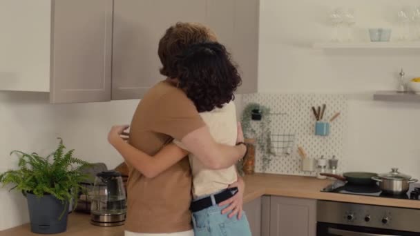 Молода пара розмовляє і обіймається, стоячи на своїй охайній кухні - Кадри, відео