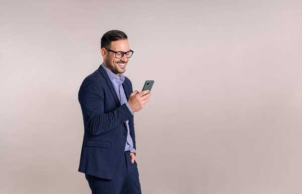 Gülümseyen yakışıklı genç girişimci beyaz arka planla cep telefonundan e-postaları kontrol ediyor - Fotoğraf, Görsel
