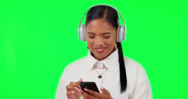 Mutlu kadın, kulaklıklar ve yeşil ekranda müzik dinleyen telefon stüdyonun arka planında. Kulaklığı ve cep telefonu uygulaması olan sakin bir kadın sesi veya ses kaydı için. - Video, Çekim