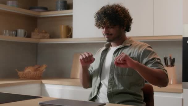 Happy Hispanic man Indian male Arabian guy enjoying finish work day success celebrating online win achieve dancing listen music celebrate accomplished work with computer closed laptop at home kitchen - Footage, Video