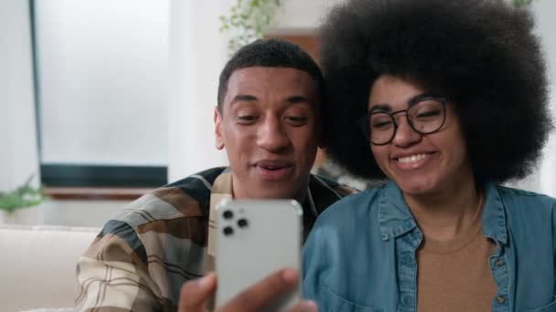 Ευτυχισμένο Αφρικής Αμερικής χαμογελαστό ζευγάρι άντρας γυναίκα στο σπίτι ανέμελη ομιλία στο κινητό τηλέφωνο κάμερα εγγραφής βίντεο ιστορίες social media bloggers vloggers influencers μιλήσει στο smartphone chat συνέδριο - Πλάνα, βίντεο