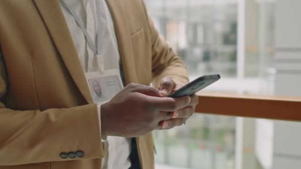 Onherkenbare zwarte man in formeel pak staat in gang met natuurlijk licht sms 'jes in zijn smartphone - Video