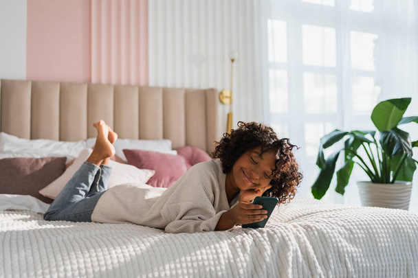 African girl holding smartphone touch screen typing scroll page at home. Woman with cell phone surfing internet using social media apps playing game. Shopping online Internet news cellphone addiction - Photo, image