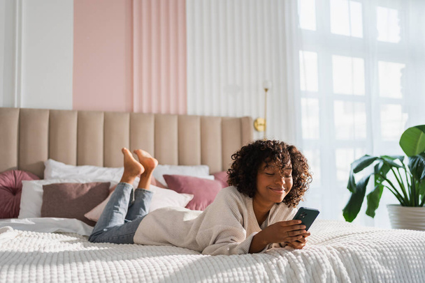 African girl holding smartphone touch screen typing scroll page at home. Woman with cell phone surfing internet using social media apps playing game. Shopping online Internet news cellphone addiction - Foto, imagen