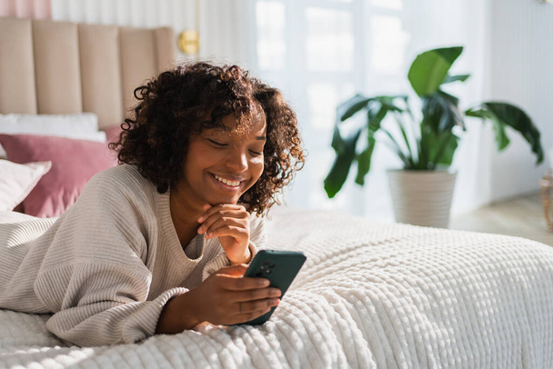 African girl holding smartphone touch screen typing scroll page at home. Woman with cell phone surfing internet using social media apps playing game. Shopping online Internet news cellphone addiction - Valokuva, kuva