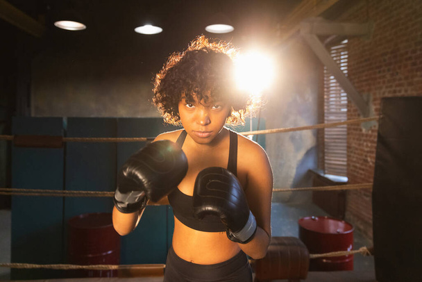 Prokřik nezávislé dívčí moci. Naštvaná africká americká bojovnice s boxerskými rukavicemi vypadá vážně agresivně stojící na boxerském ringu. Silný silný bojovník dívka trénink rány - Fotografie, Obrázek