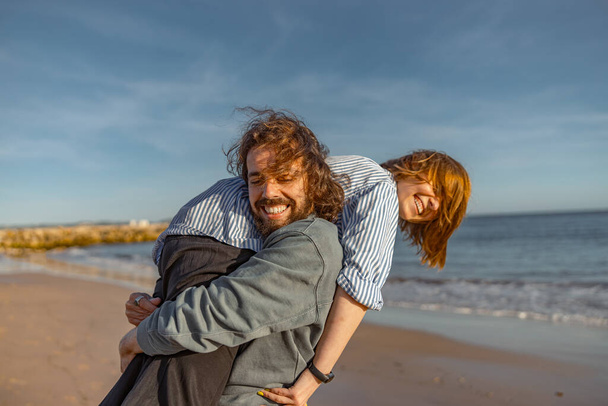 Улыбчивая пара дурачится во время прогулки по пляжу в солнечный ветреный день. Высокое качество фото - Фото, изображение
