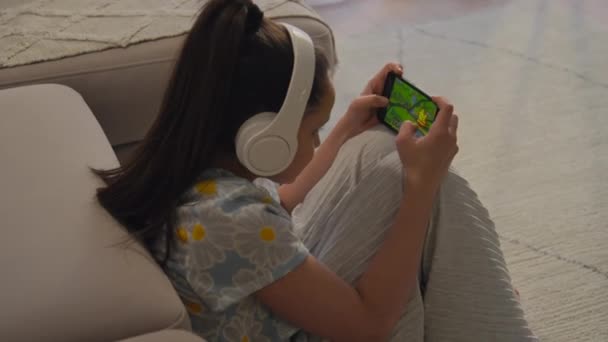 Alto angolo colpo di giovane ragazza moderna seduta accanto al divano sentirsi felici dopo aver vinto nel gioco online sul suo smartphone - Filmati, video