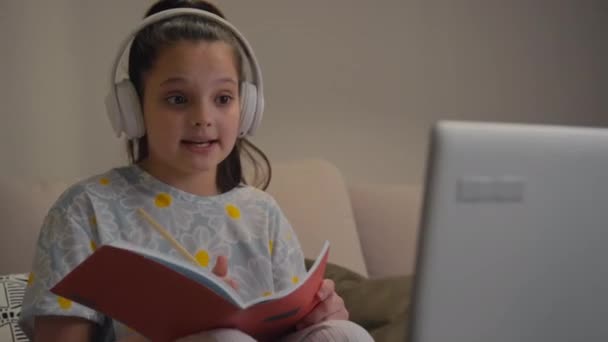 Teenage κορίτσι φορώντας λευκά ακουστικά ζητώντας σε απευθείας σύνδεση ερώτηση δάσκαλος της, ενώ οι σπουδές από το σπίτι - Πλάνα, βίντεο