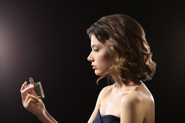 Beautiful woman with perfume bottle on dark background - Fotó, kép