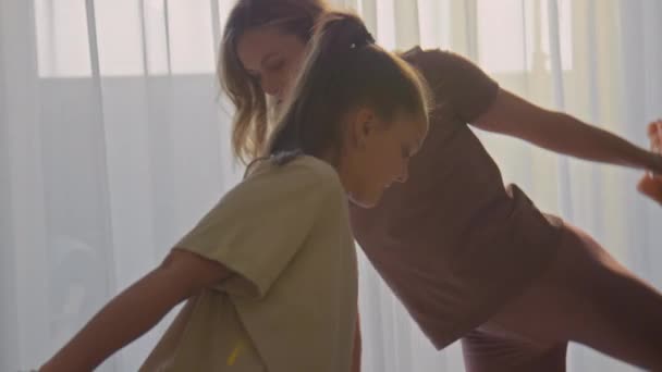 Tilt κάτω πυροβολισμό της μικρής οικογένειας της μητέρας και της κόρης κάνει ασκήσεις τεντώματος στην άνεση του σαλονιού τους - Πλάνα, βίντεο