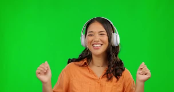 Dancing, music headphones and woman on green screen in studio isolated on a background. Radio, listening and happy Asian person streaming audio, sound or podcast, jazz playlist and dance with energy - Footage, Video