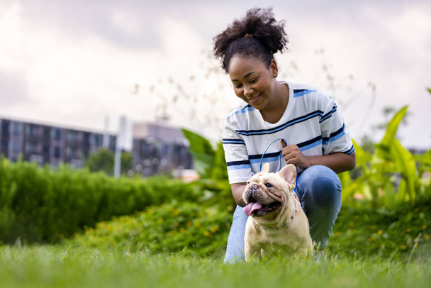アフリカ系アメリカ人の女性は公園で朝の運動をした後に芝生の芝生に横になっている間、彼女のフランスのブルドッグ子犬と遊んでいます - 写真・画像