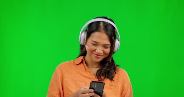 Muziek koptelefoon, telefoon en vrouw op groen scherm in studio geïsoleerd op een achtergrond mockup. Radio, luisteren en Aziatische persoon met smartphone voor het typen, scrollen op sociale media of streaming podcast - Video
