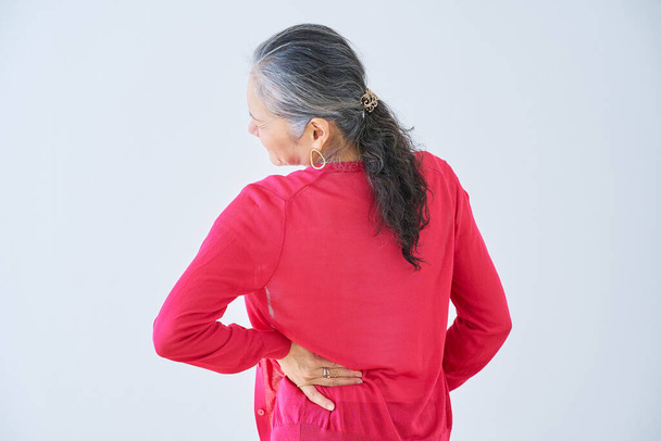 Οπίσθια όψη ηλικιωμένης γυναίκας που υποφέρει από πόνο στην πλάτη σε εσωτερικούς χώρους - Φωτογραφία, εικόνα