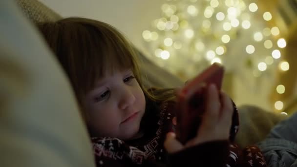 A gyerek rajzfilmeket néz a telefonon lefekvés előtt. A lány elalszik egy kütyüvel a kezében. Kiváló minőségű 4k felvételek - Felvétel, videó