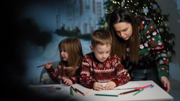 Οικογενειακές Γιορτές: Η Μητέρα Βοηθά Τα Παιδιά Να Γράφουν Γράμματα Στον Άγιο Βασίλη, Περιτριγυρισμένο από το Χριστουγεννιάτικο Δέντρο. Υψηλής ποιότητας 4k πλάνα - Πλάνα, βίντεο