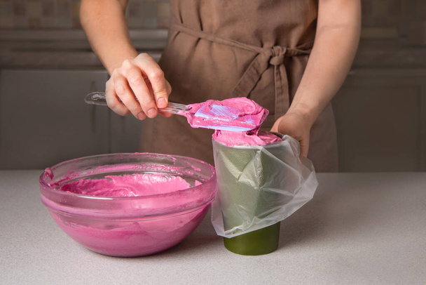 Kadın pasta şefi pastalar için pembe hamuru mutfaktaki pasta çantasına koydu. - Fotoğraf, Görsel