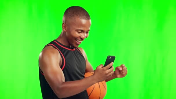 Kosárlabda, győztes és fekete férfi telefonnal a zöld képernyőn a stúdióban elszigetelt háttérképpel. Ünnep, mobil és sportoló labdával nyertes díjat, siker vagy izgatott vicces sportok. - Felvétel, videó