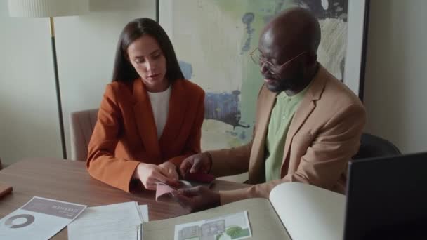 Επαγγελματική σχεδιάστρια που βοηθά τον πελάτη της να αποφασίσει νέα χρωματική παλέτα για το σπίτι του με τη βοήθεια δειγμάτων υφασμάτων - Πλάνα, βίντεο